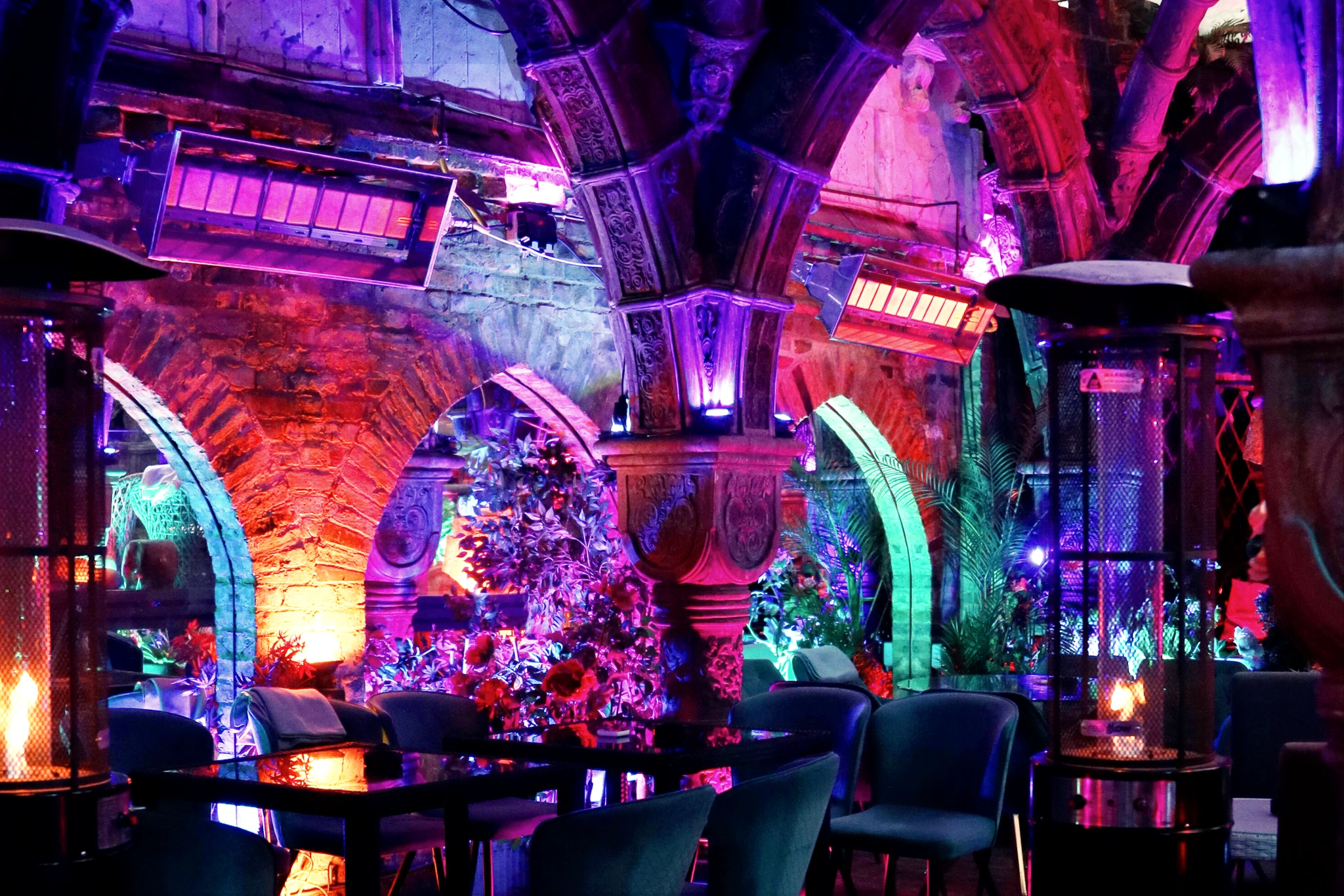An ornate central column and carved garden arches illuminated in violet, pink and amber above the dining tables