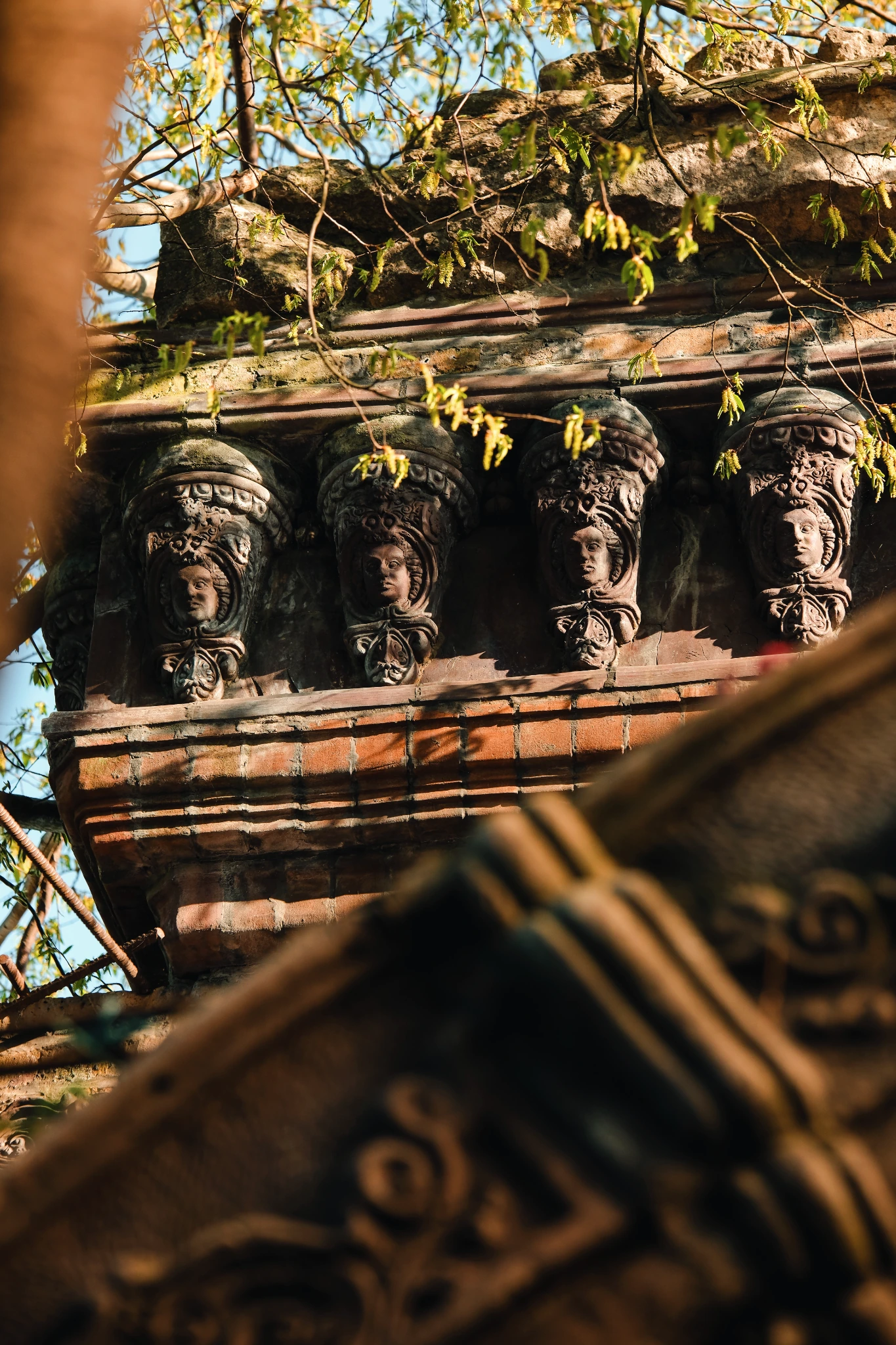 Sculpted faces and decorative garden stonework framed by sunlit leaves