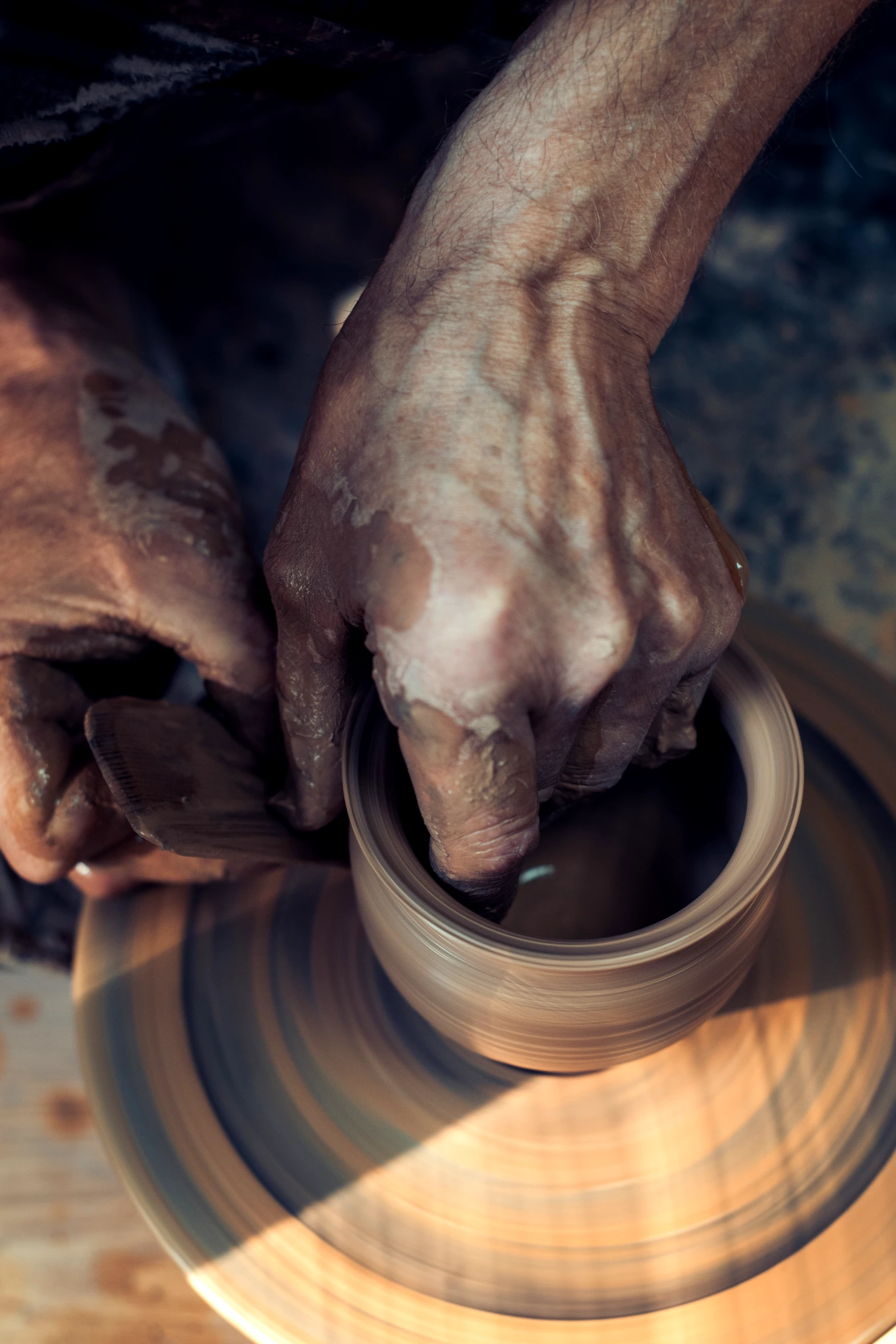 Hands carefully shaping a clay pot on a turning pottery wheel