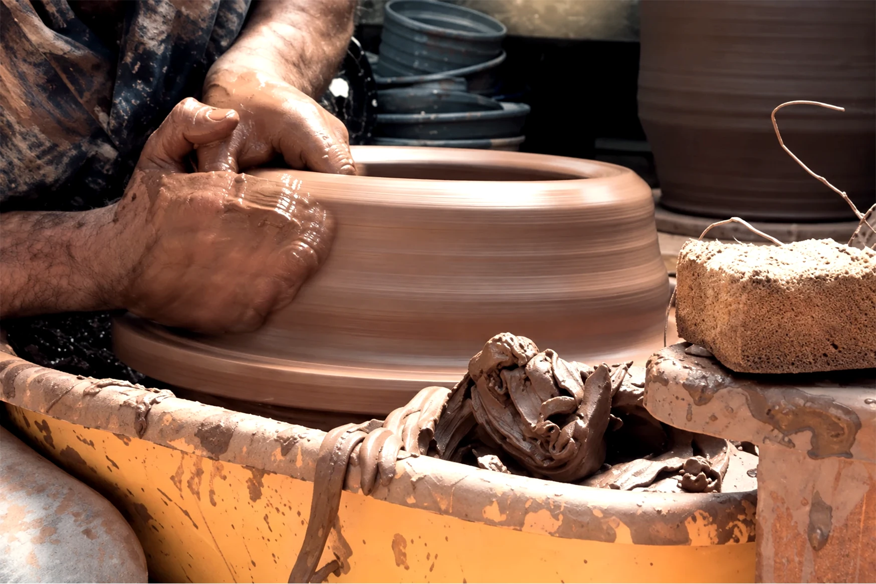 The owner’s hands shaping a large clay vessel on the pottery wheel