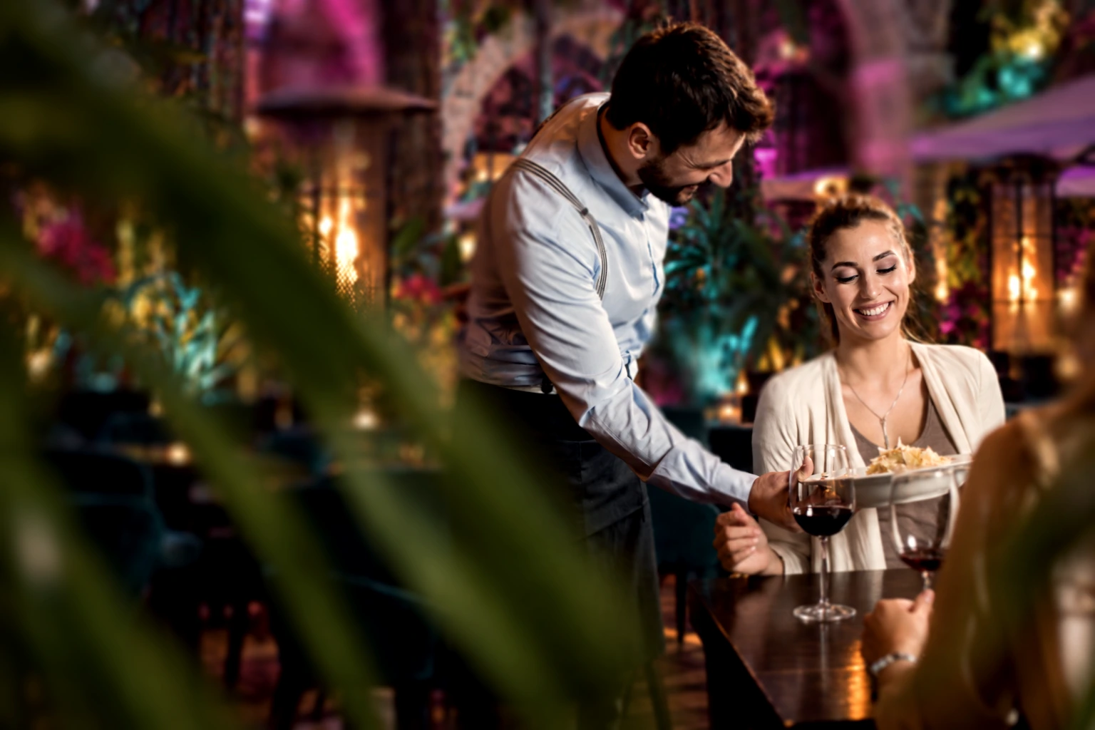 A waiter serving a meal to a smiling guest in the warmly lit Garden