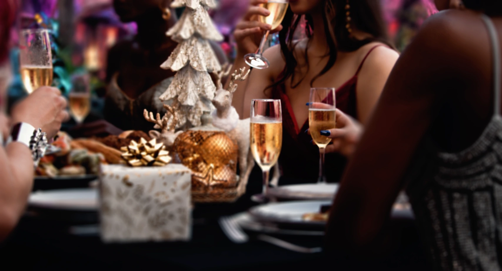 Guests sharing a festive meal around a Christmas table with champagne, gifts and a silver tree centrepiece