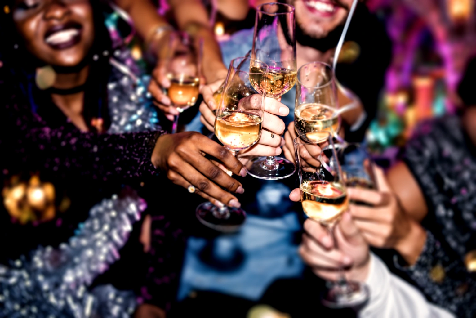 Friends raising champagne glasses for a New Year celebration beneath colourful party lights