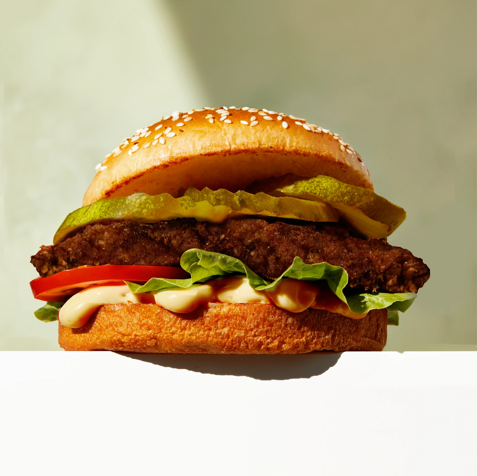 A burger with cheese, lettuce and tomato in a sesame bun