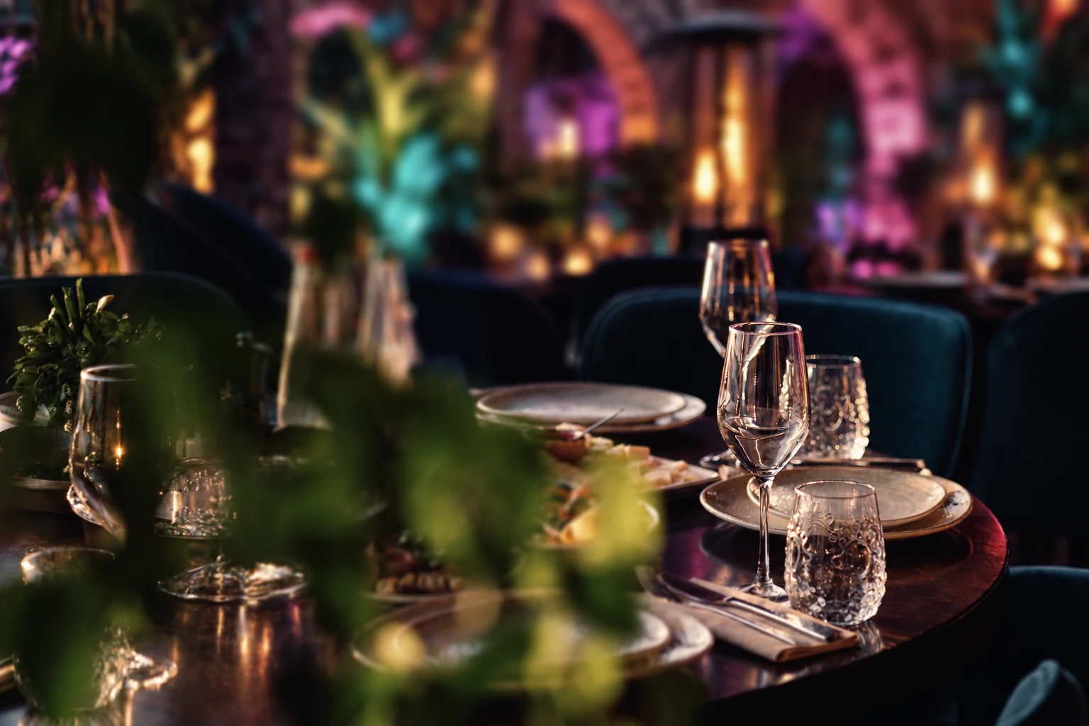 An elegantly laid garden table with glasses, candles and leafy surroundings